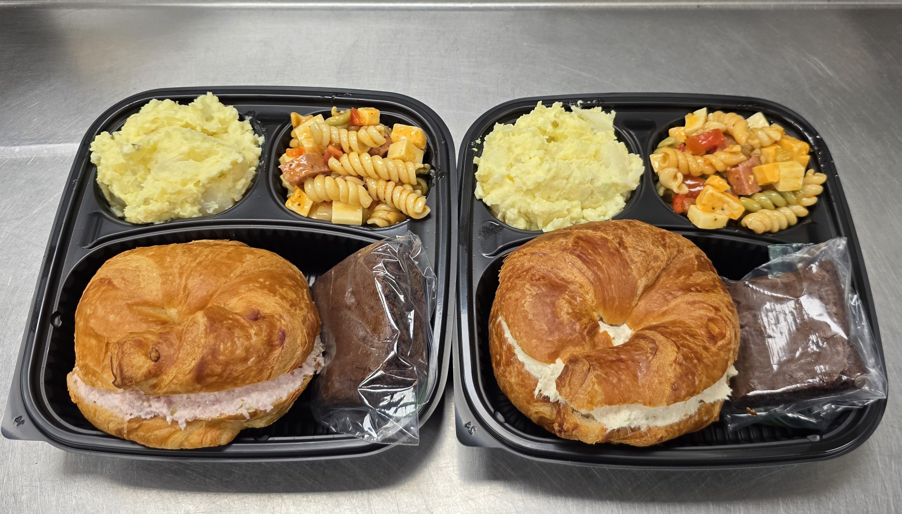 Two meal trays with croissant sandwiches and sides